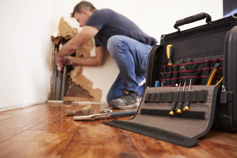 plumber repairing leak from a burst pipe behind resident's wall